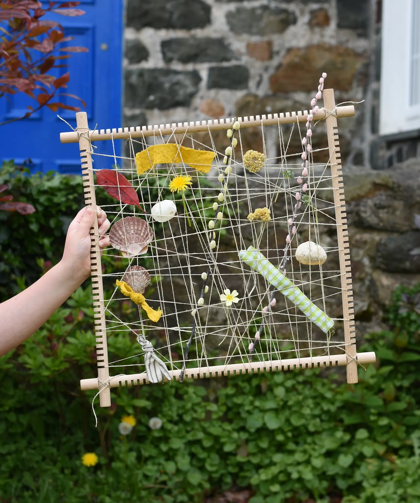 Grapat weaving frame built and filled with natural material including laves, flowers, pussy willow branches and material scraps.