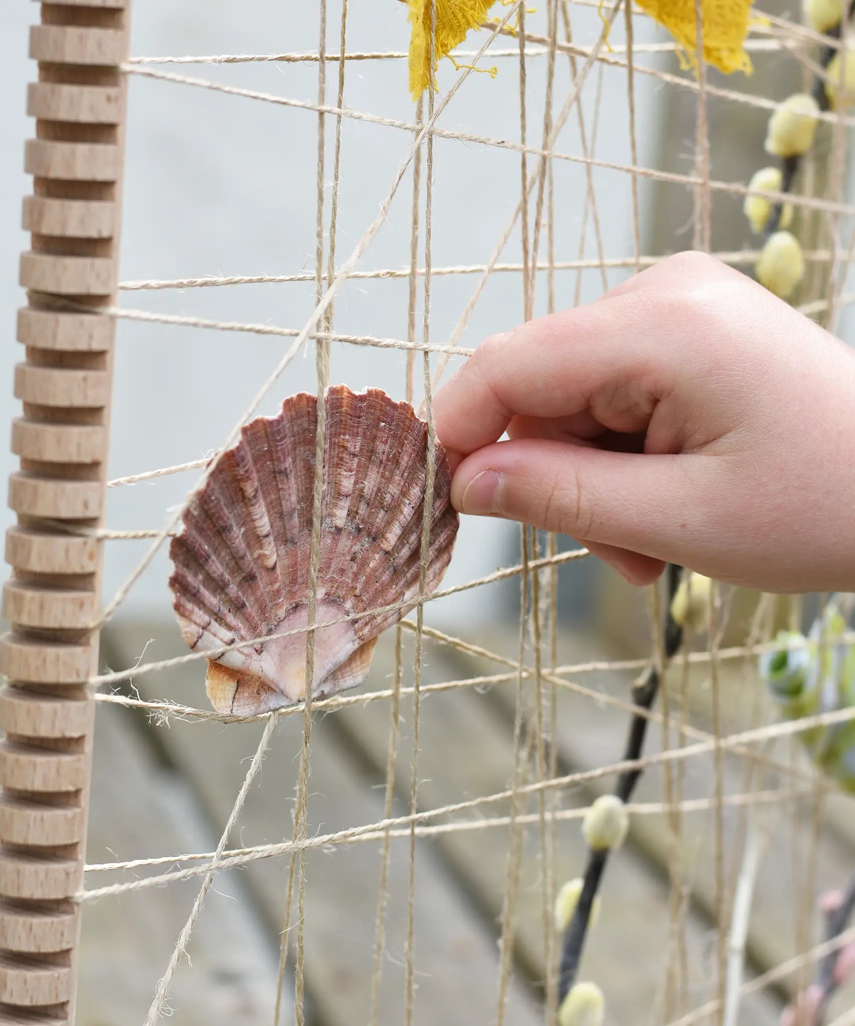 Child's hand placing a shell into the Grapat weaving frame.