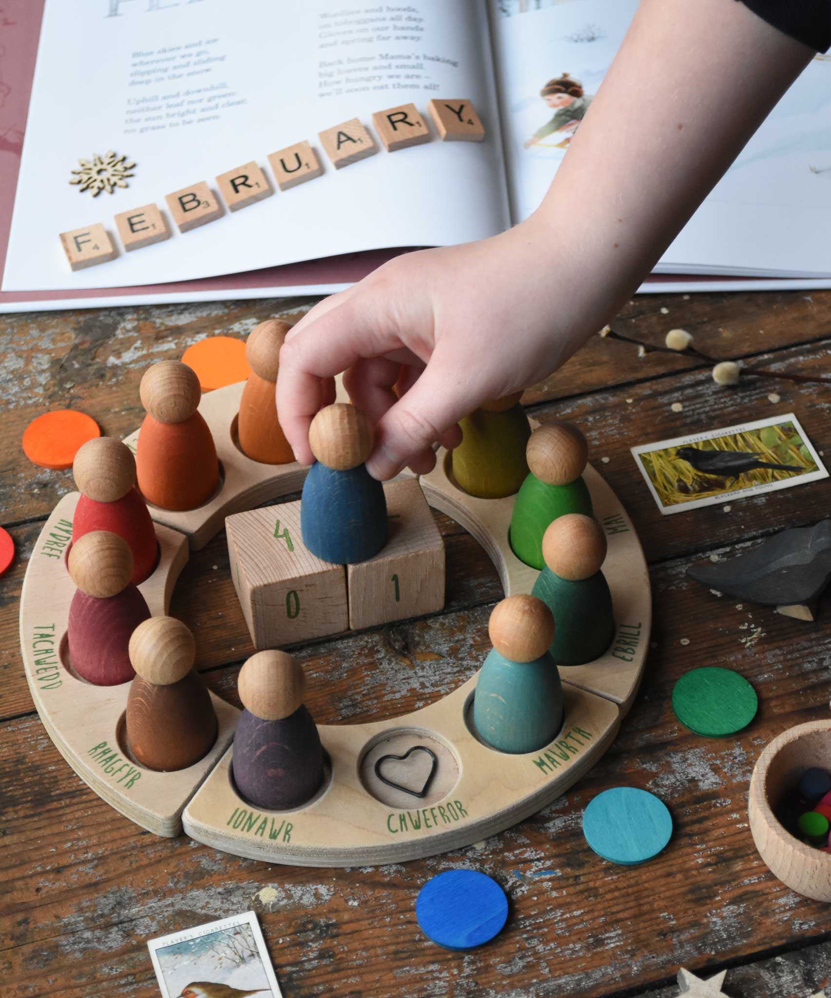 Child placing the blue Nin from the Grapat Welsh perpetual calendar on top of the date number blocks. 