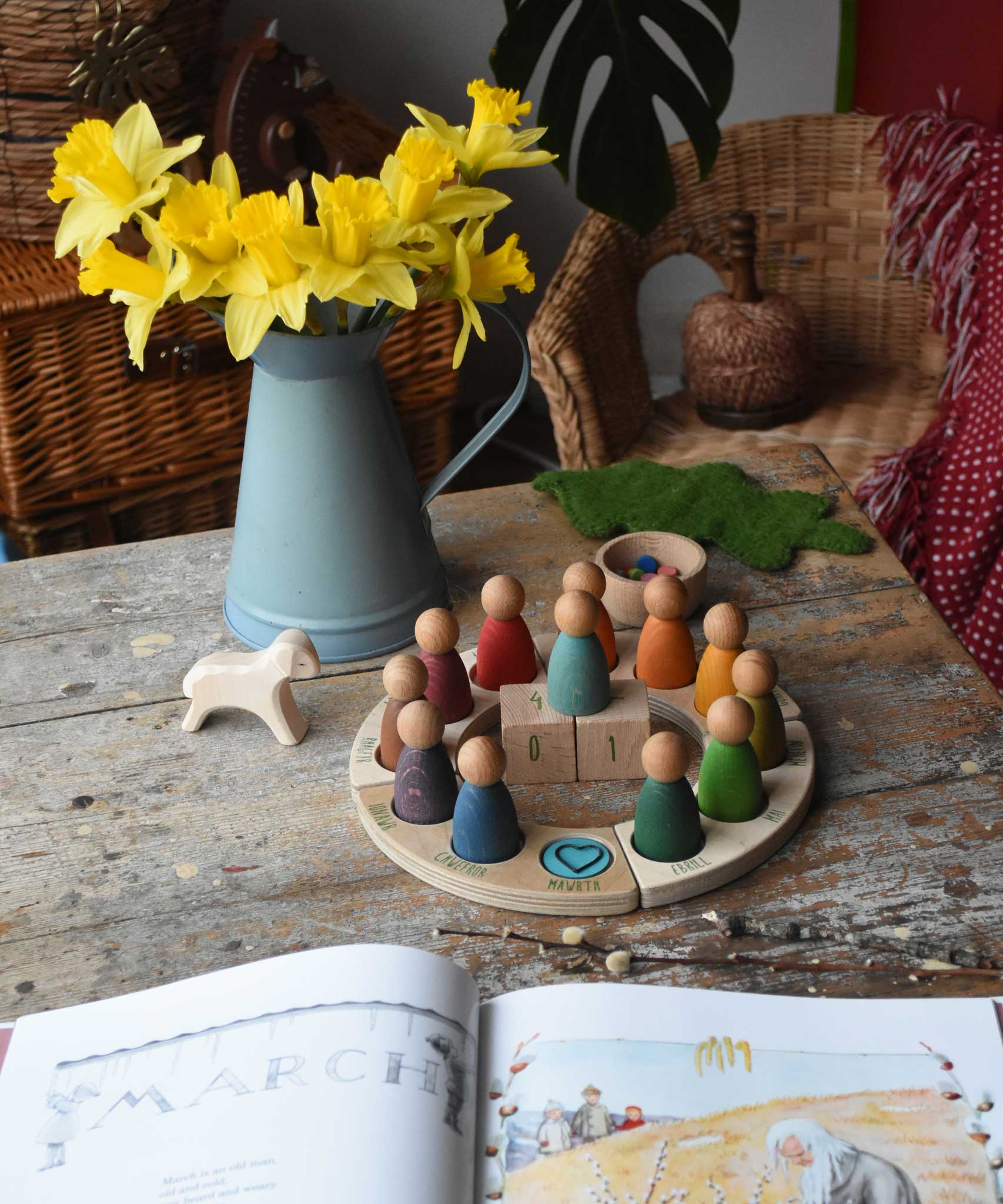 The Grapat Welsh perpetual calendar set up on a wooden surface showing March the 1st as a date. A bunch of daffodils cane be seen just behind it.