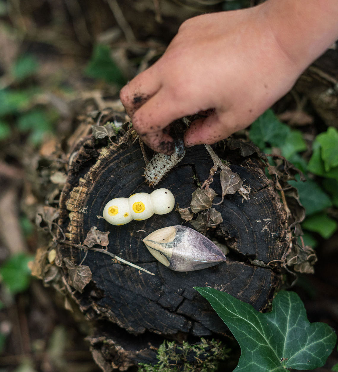 A child's hand holding a bug next to two pieces from the Grapat wooden wild creatures set. Grapat have a wide range of wooden toys and loose parts available at Babipur. 