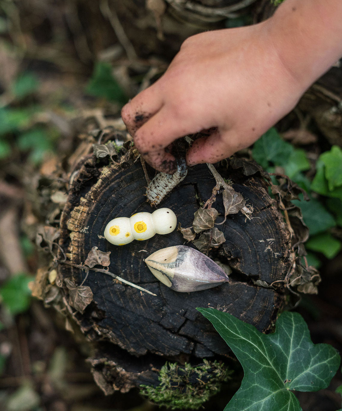 A child's hand holding a bug next to two pieces from the Grapat wooden wild creatures set. Grapat have a wide range of wooden toys and loose parts available at Babipur. 