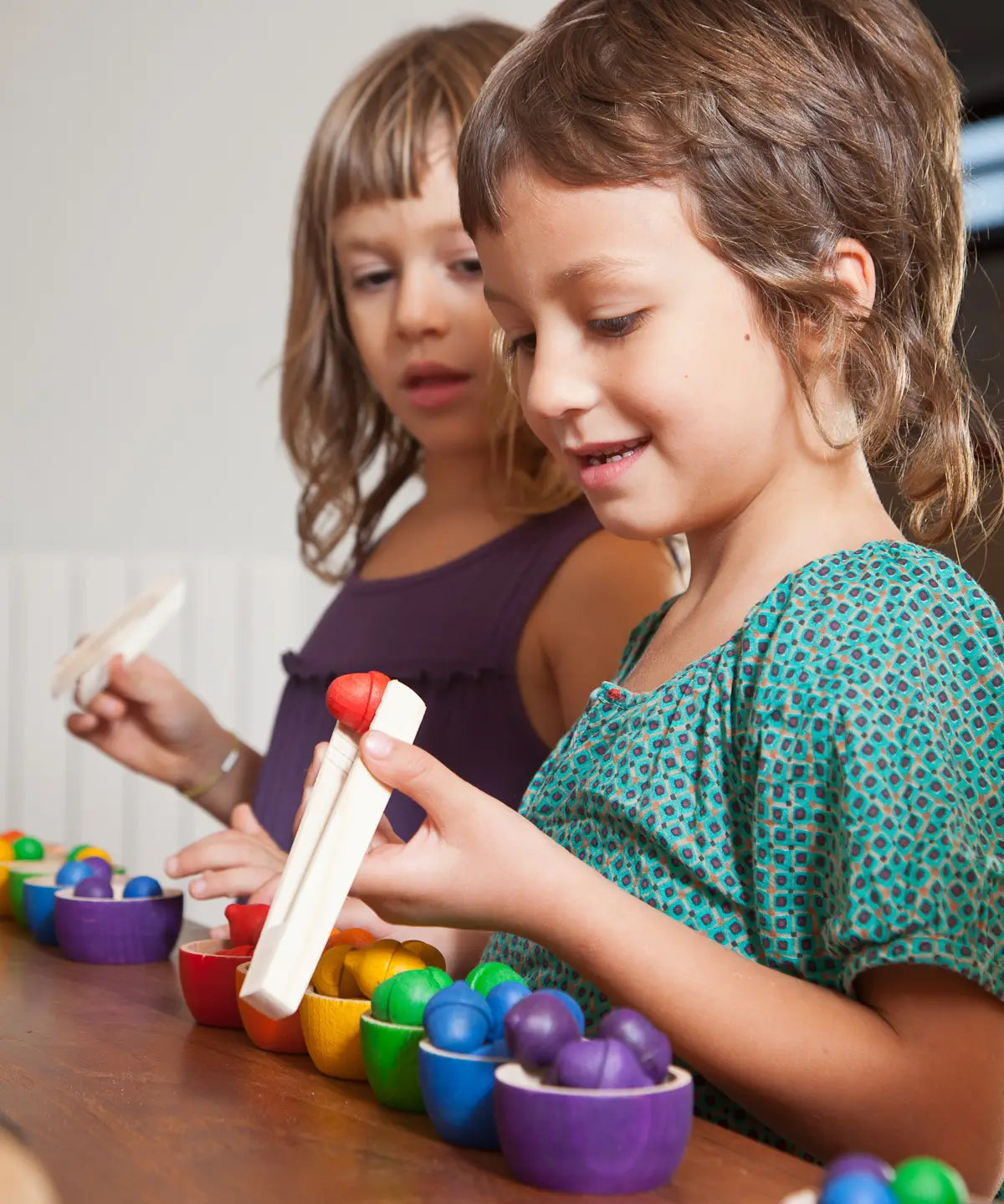 Children sorting Grapat wooden acorn loose pieces with tweezers into matching coloured handcrafted wooden bowls