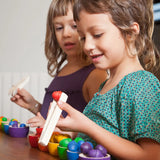 Children sorting Grapat wooden acorn loose pieces with tweezers into matching coloured handcrafted wooden bowls