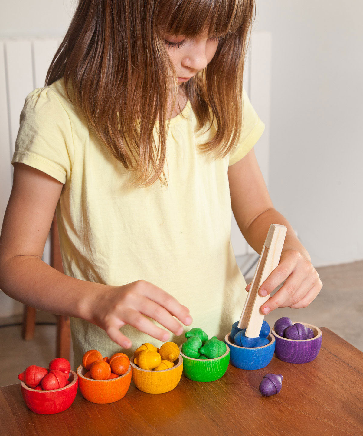 A child playing with the Grapat Wooden Toy Bowls and  Acorns Set. A set of 6 coloured bowls with wooden acorn shapes in matching pieces. These wooden toys are part of a wide range of open ended toys available at Babipur.  