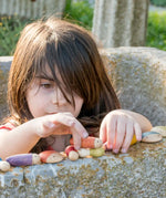 Child stacking different long Grapat insect pieces on a concrete wall