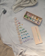 and small colourful cubes in various colors. The lid of the box has small painted dots in various colours and is on a white background