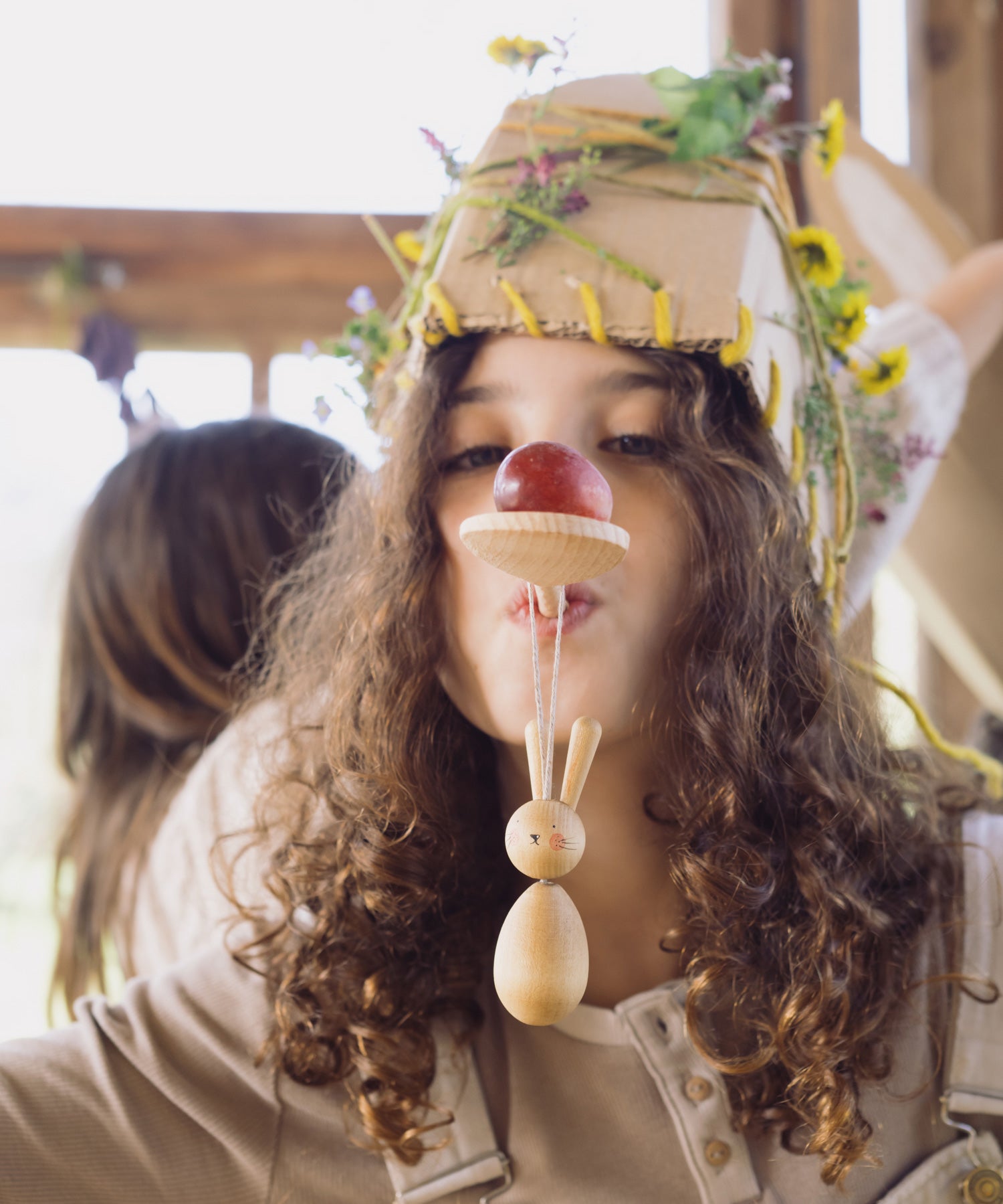 A child with a wooden spoon on their mouth with the bunny decoration looped on the handle. 