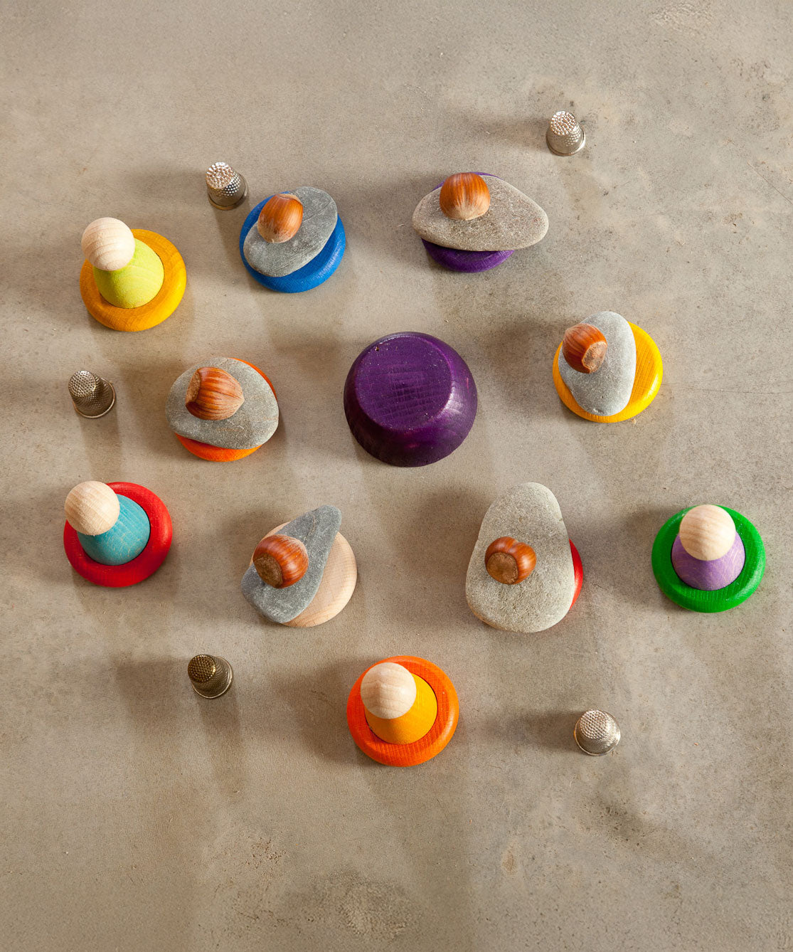 A selection of wooden toys from Grapat including Nins, wooden bowls and rings placed on the floor. Some have stones balanced on them.  