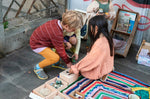 2 children crouched down reaching into the Grapat wooden permanence toy box