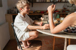 Child sitting on a chair next to a kitchen table holding  a orange and light green Grapat handcrafted, painted puppets in the hand