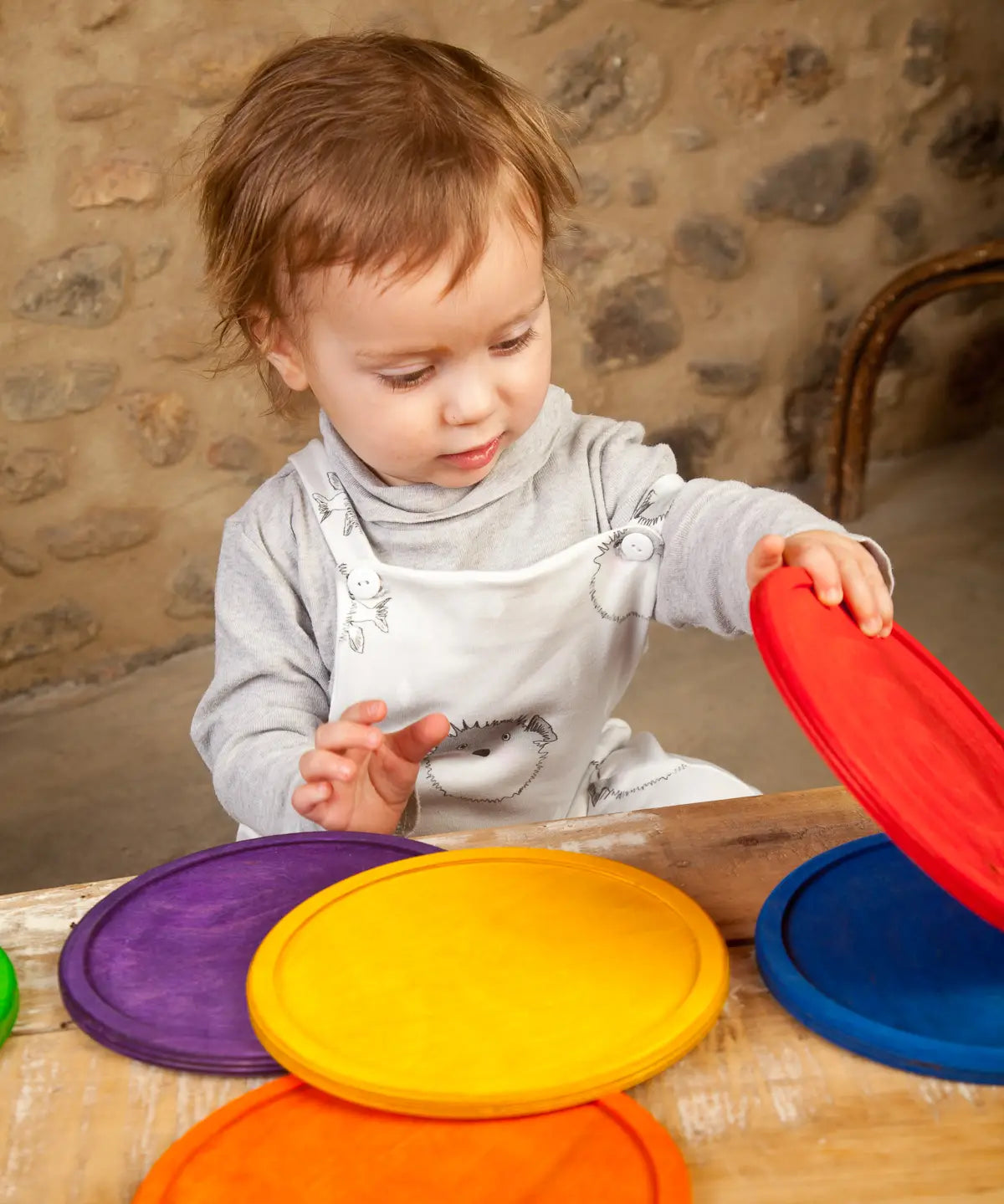 Child holding Grapat's handcrafted wooden rainbow dish pieces on a table