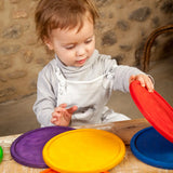 Child holding Grapat's handcrafted wooden rainbow dish pieces on a table