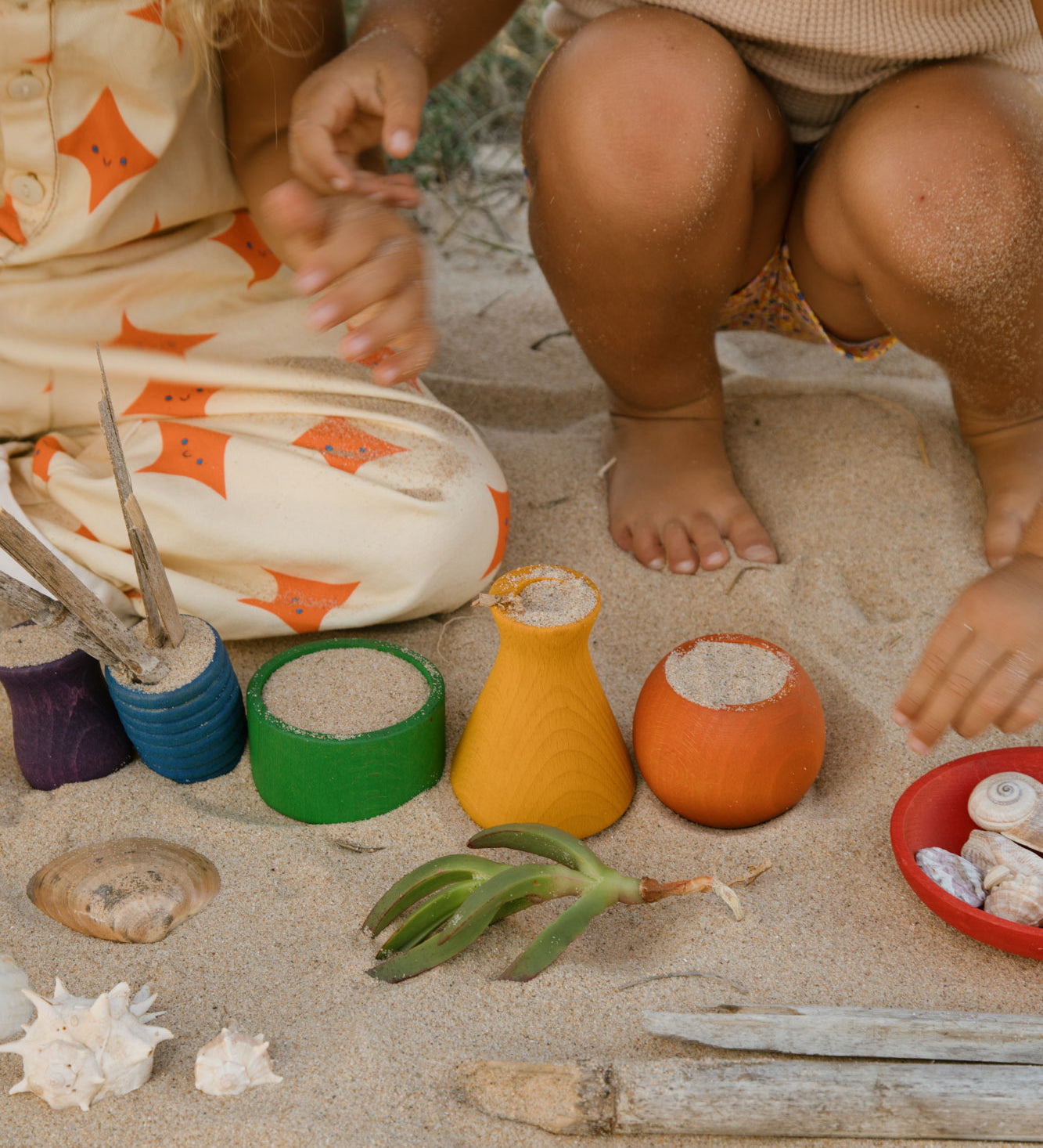 Children playing with the Grapat Wooden Rainbow Sorting Pots on teh sand. Wooden pots in a mix of shapes in different colours.