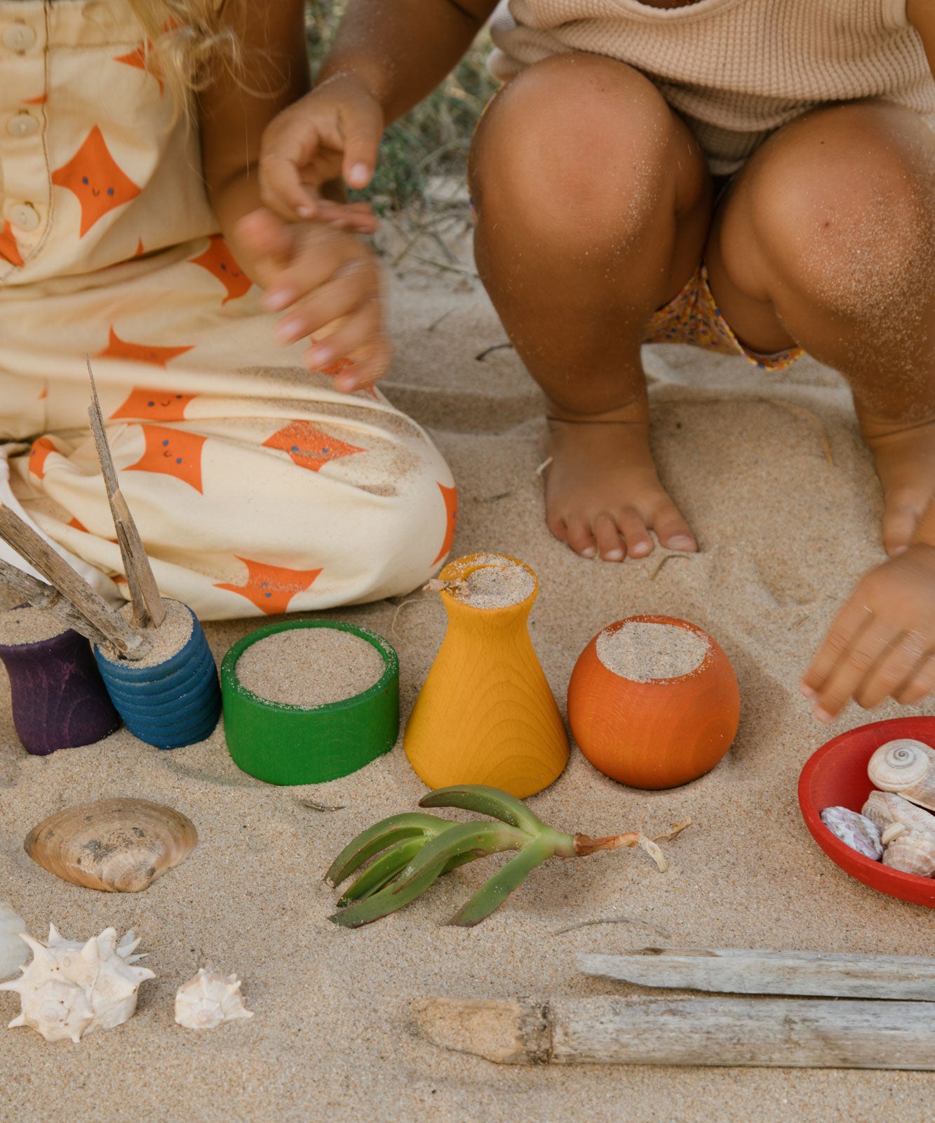 Children playing with the Grapat Wooden Rainbow Sorting Pots on teh sand. Wooden pots in a mix of shapes in different colours.