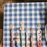 Grapat Sensory Play Tools wooden toy set. The play tools are placed on a blue and white gingham tablecloth.