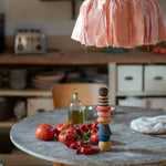 The Grapat serendipity wooden stacking set stacked on a dining table next to chillies, tomatoes and olive oil. Features handcrafted brown, light pink, blue yellow orange and striped pieces. 
