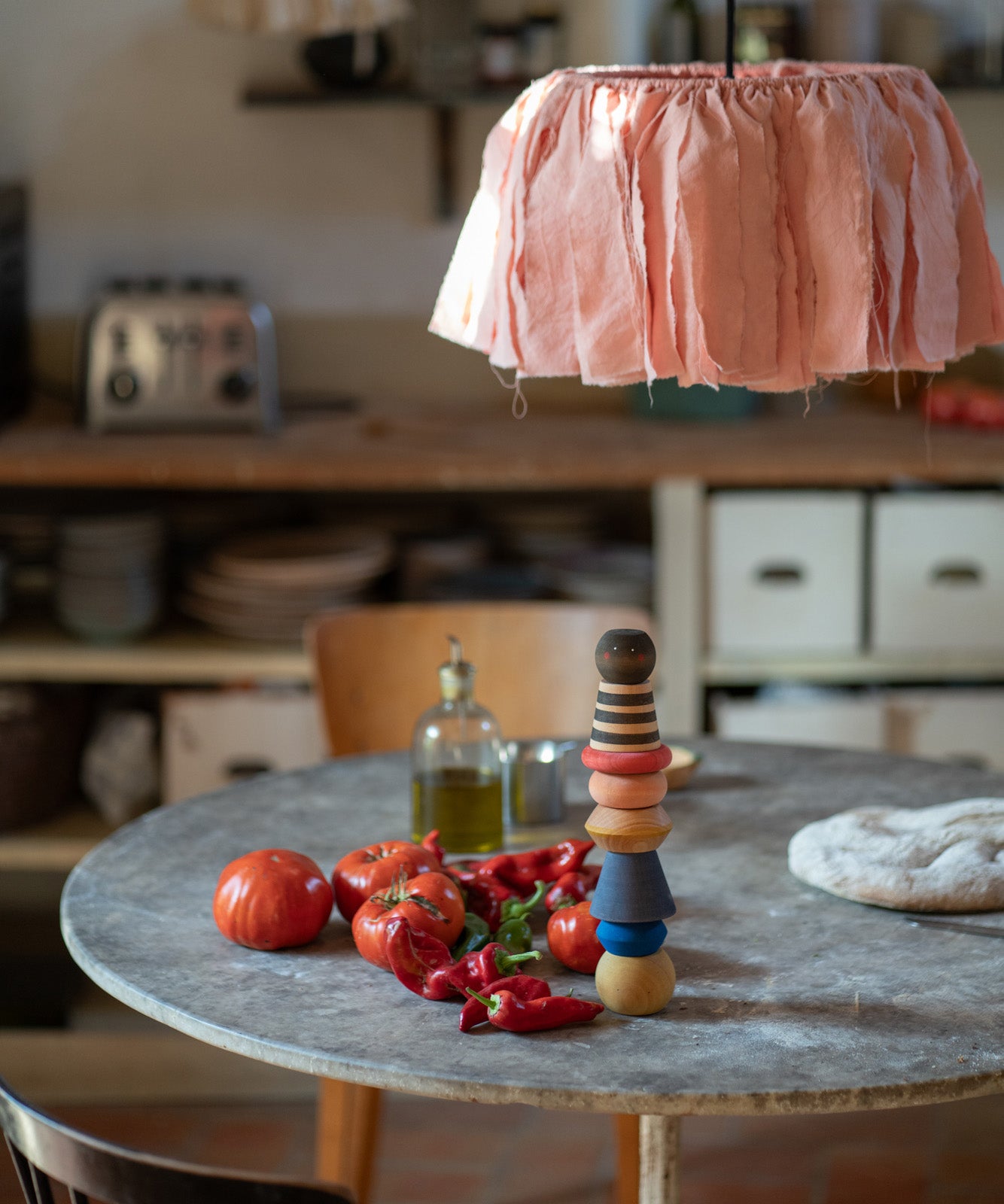 The Grapat serendipity wooden stacking set stacked on a dining table next to chillies, tomatoes and olive oil. Features handcrafted brown, light pink, blue yellow orange and striped pieces. 