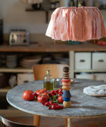 The Grapat serendipity wooden stacking set stacked on a dining table next to chillies, tomatoes and olive oil. Features handcrafted brown, light pink, blue yellow orange and striped pieces. 