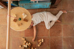 A child lying on a terracotta floot under the Grapat wooden pendulum set with wooden blocks on the floor