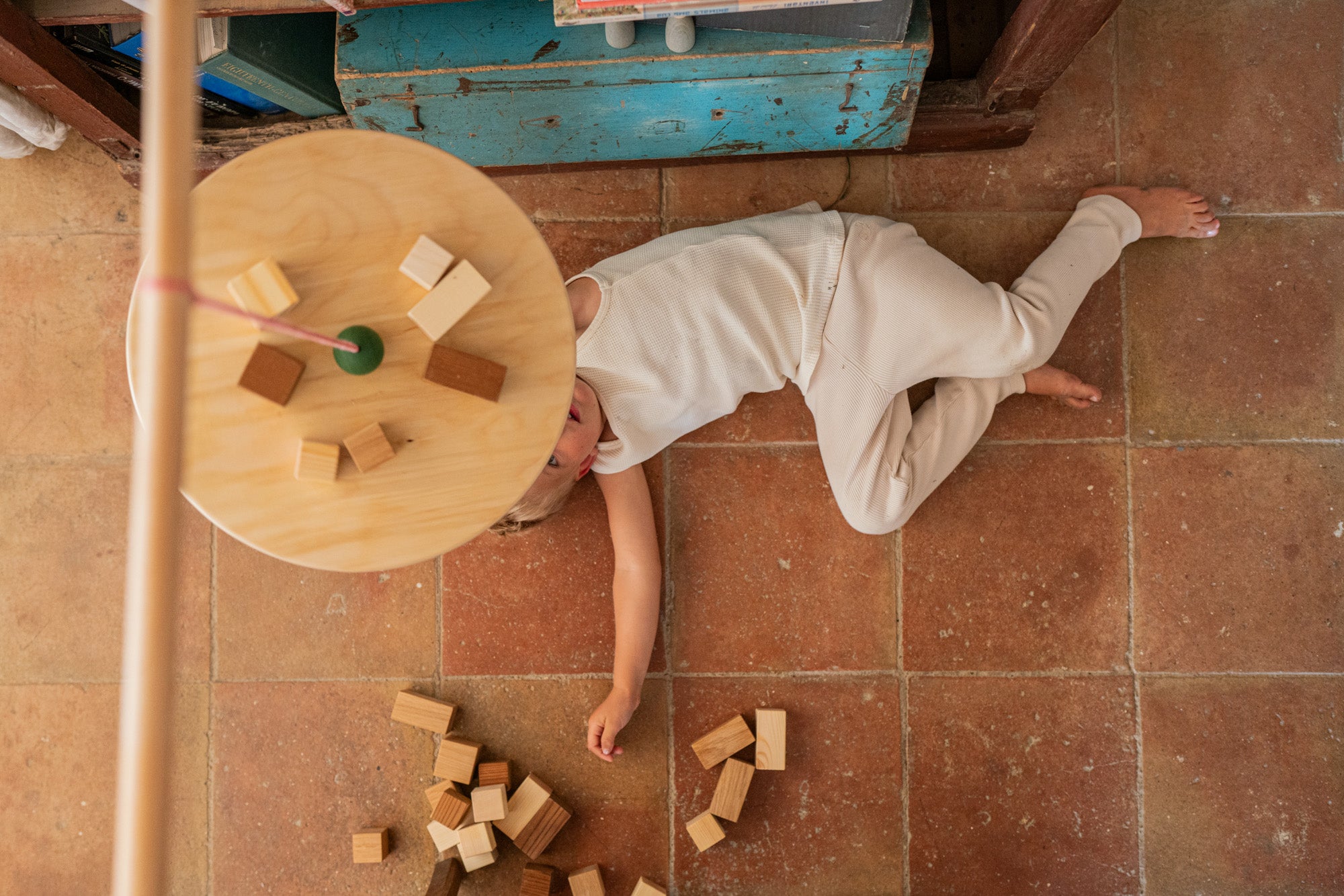 A child lying on a terracotta floot under the Grapat wooden pendulum set with wooden blocks on the floor
