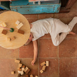 A child lying on a terracotta floot under the Grapat wooden pendulum set with wooden blocks on the floor