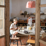Child sitting next to the kitchen table playing with the Grapat handcrafted wooden puppets with 4 puppets resting on the wooden stand.