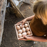 A child holding the Grapat square shaped Wooden Storage Box filled with eggs. 
