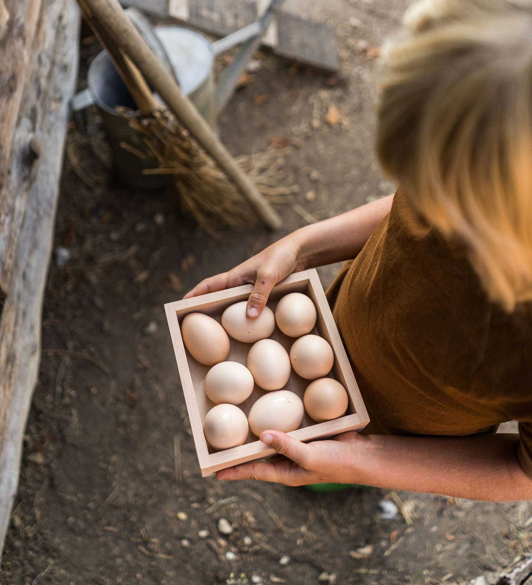 A child holding the Grapat square shaped Wooden Storage Box filled with eggs. 