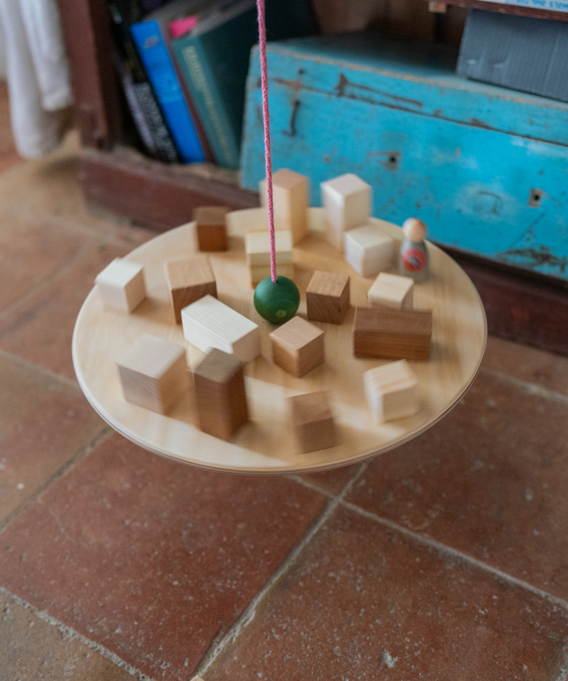 Grapat wooden pendulum set with wooden blocks on the balancing on the wooden balance board above a terracotta floor.