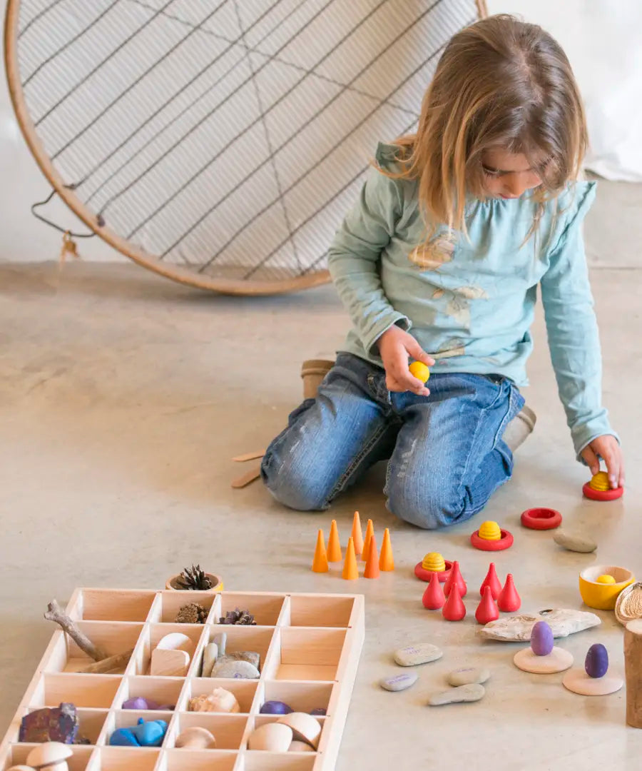 A Grapat tinker tray filled with loose pieces next to a child sorting other wooden pieces 