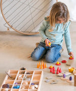 A Grapat tinker tray filled with loose pieces next to a child sorting other wooden pieces 