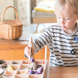 Child standing next to a a Grapat tinker tray and using tongs to fill a compartment with loose wooden pieces