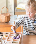 Child standing next to a a Grapat tinker tray and using tongs to fill a compartment with loose wooden pieces