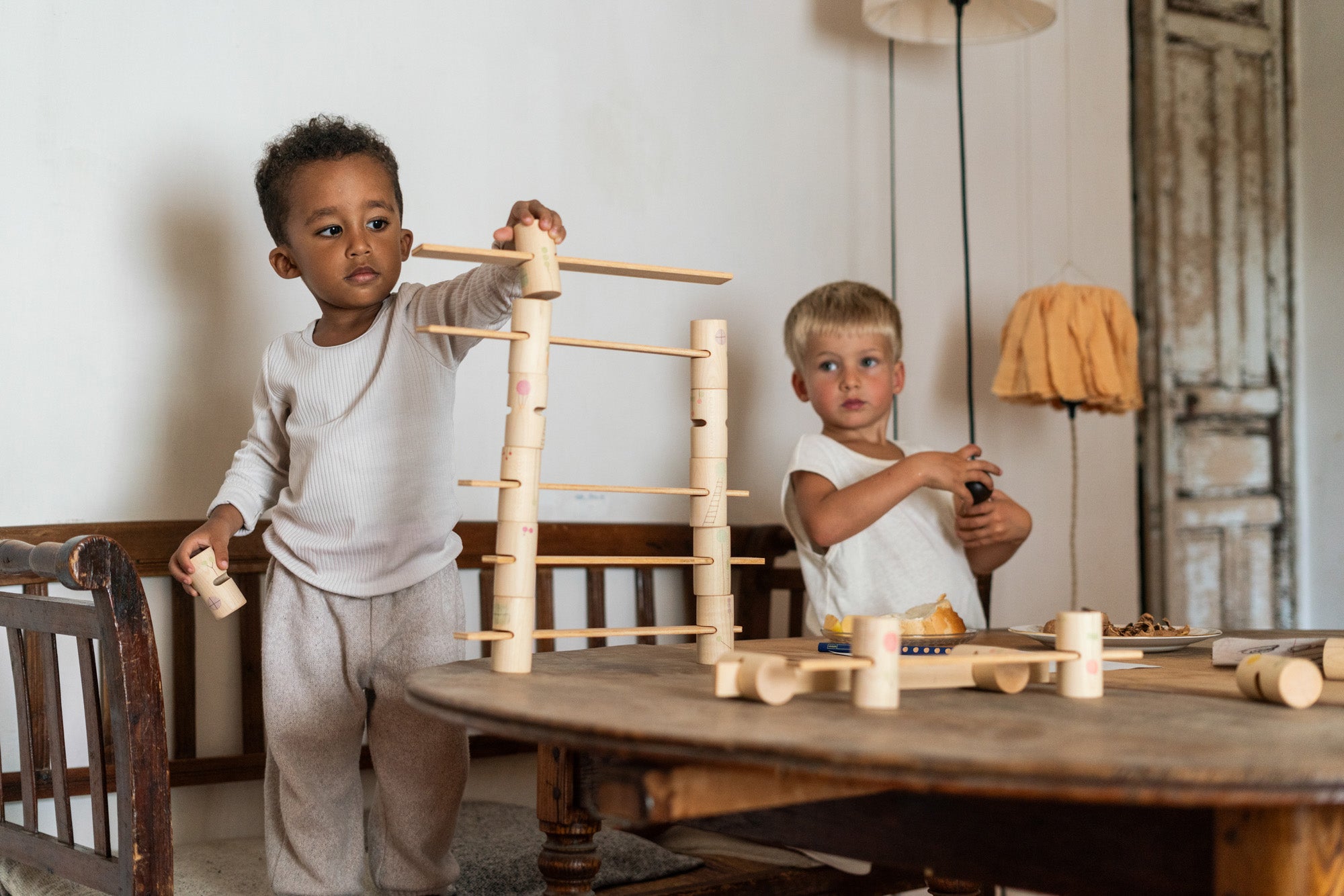 2 children sitting next to a table playing with the handcrafted, painted tubes and planks from the woodland set stacked on a wooden table