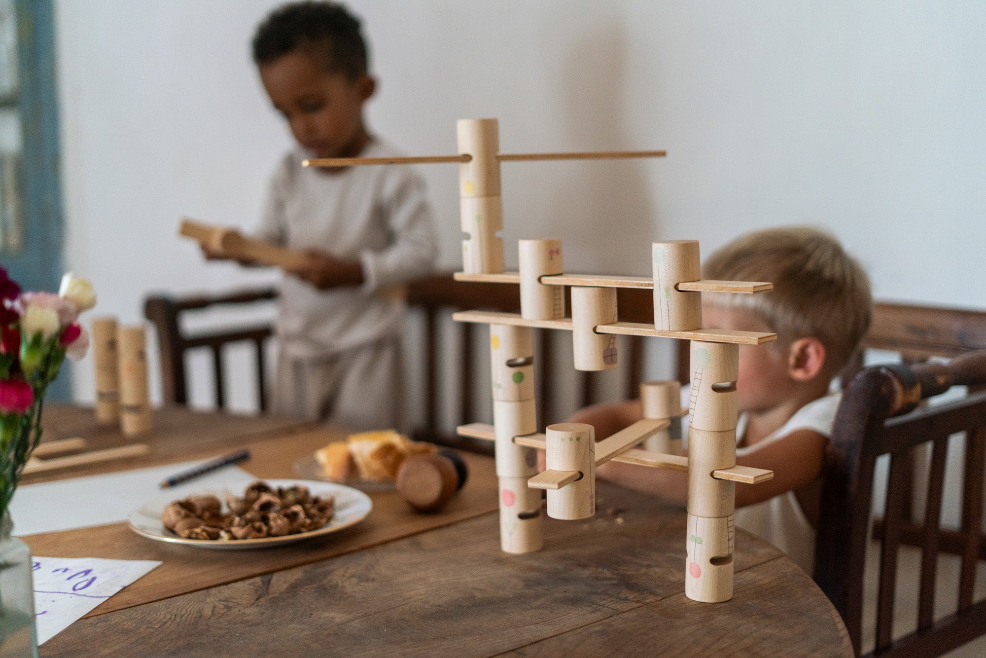 Close up of the Grapat wooden woodland set on a wooden table. Showing the different handcrafted, painted tubes and planks. Featuring painted details of windows, ladders and flowers. 