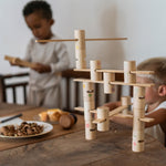 Close up of the Grapat wooden woodland set on a wooden table. Showing the different handcrafted, painted tubes and planks. Featuring painted details of windows, ladders and flowers. 