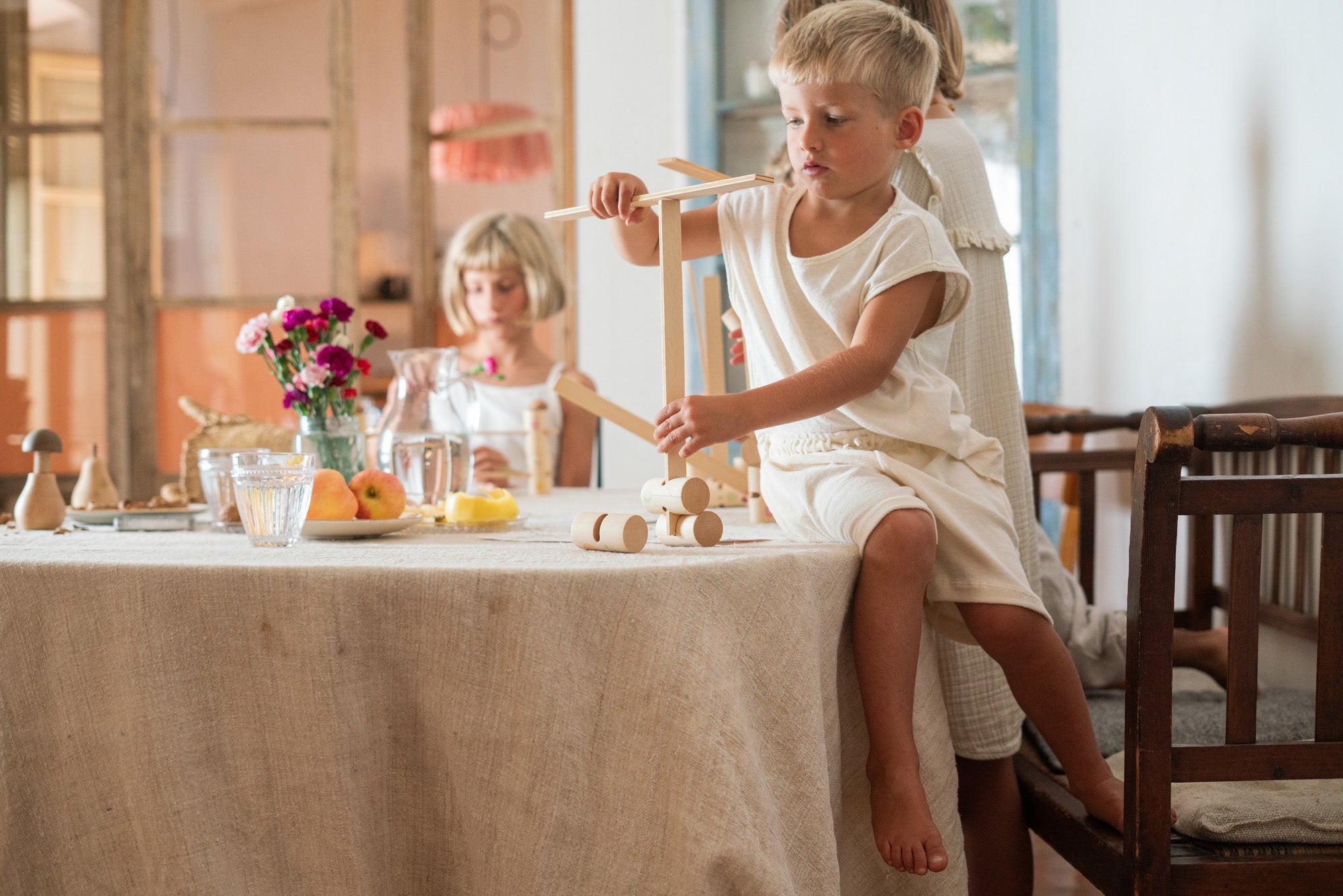 Child sitting on a dining table balancing a plank on another plank from the Grapat woodland set. 