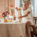 Child sitting on a dining table balancing a plank on another plank from the Grapat woodland set. 