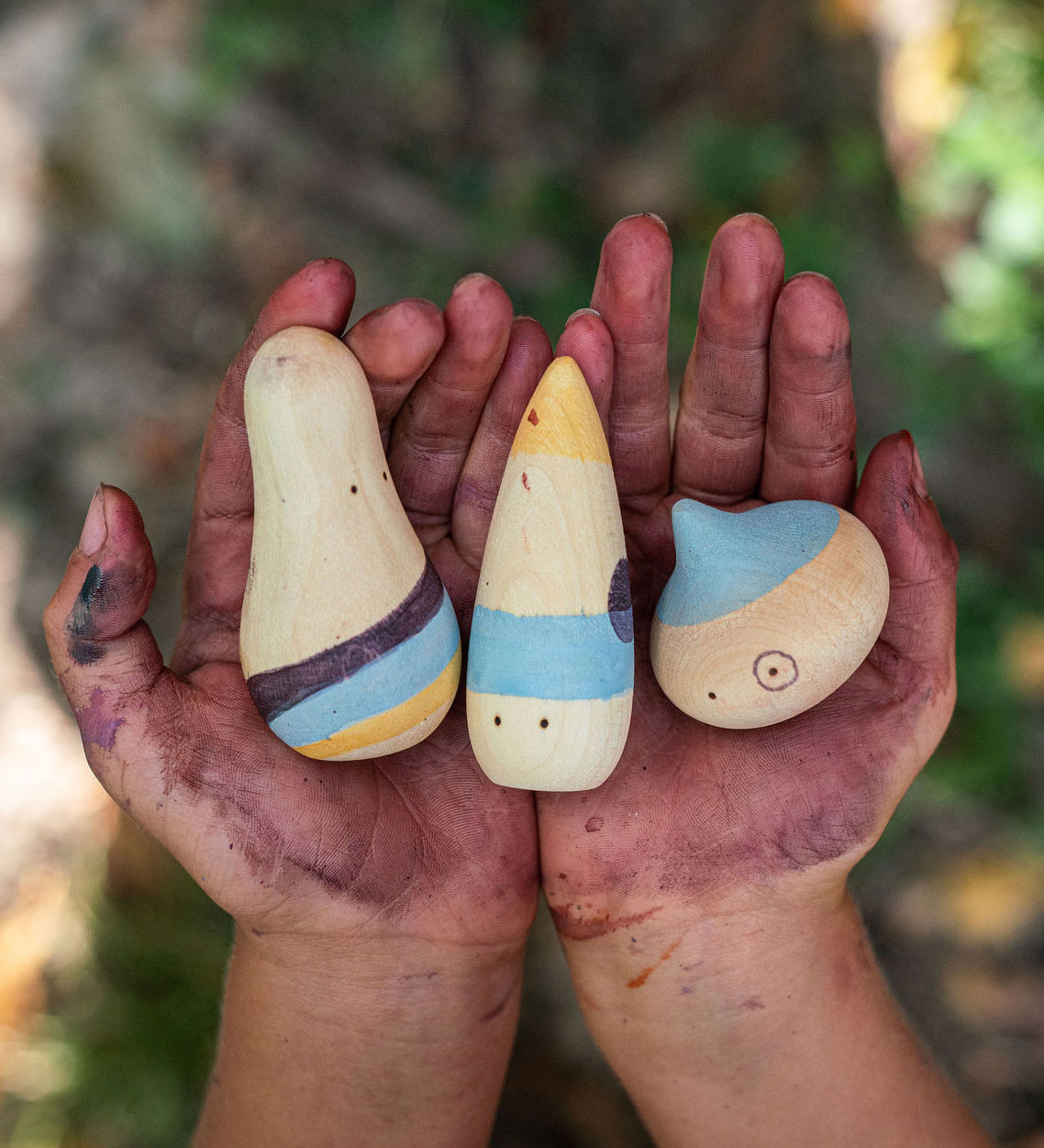 The Grapat Wow! Set shown in a child's hands. A set of three wooden toy figures hand painted in red, purple and yellow.