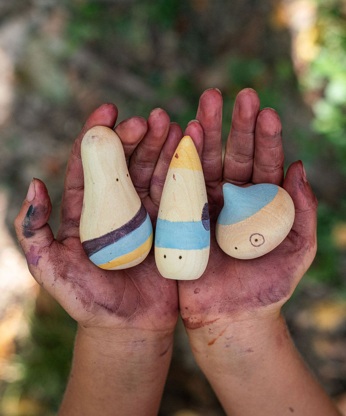 The Grapat Wow! Set shown in a child's hands. A set of three wooden toy figures hand painted in red, purple and yellow.