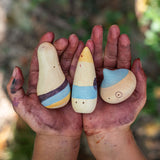 The Grapat Wow! Set shown in a child's hands. A set of three wooden toy figures hand painted in red, purple and yellow.
