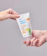 Two hand holding onto a tube of Green People Children SPF30 Sun Cream against a grey background. 