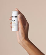 A Green People Light Tinted DD Moisturiser tube being held up against a beige background. 