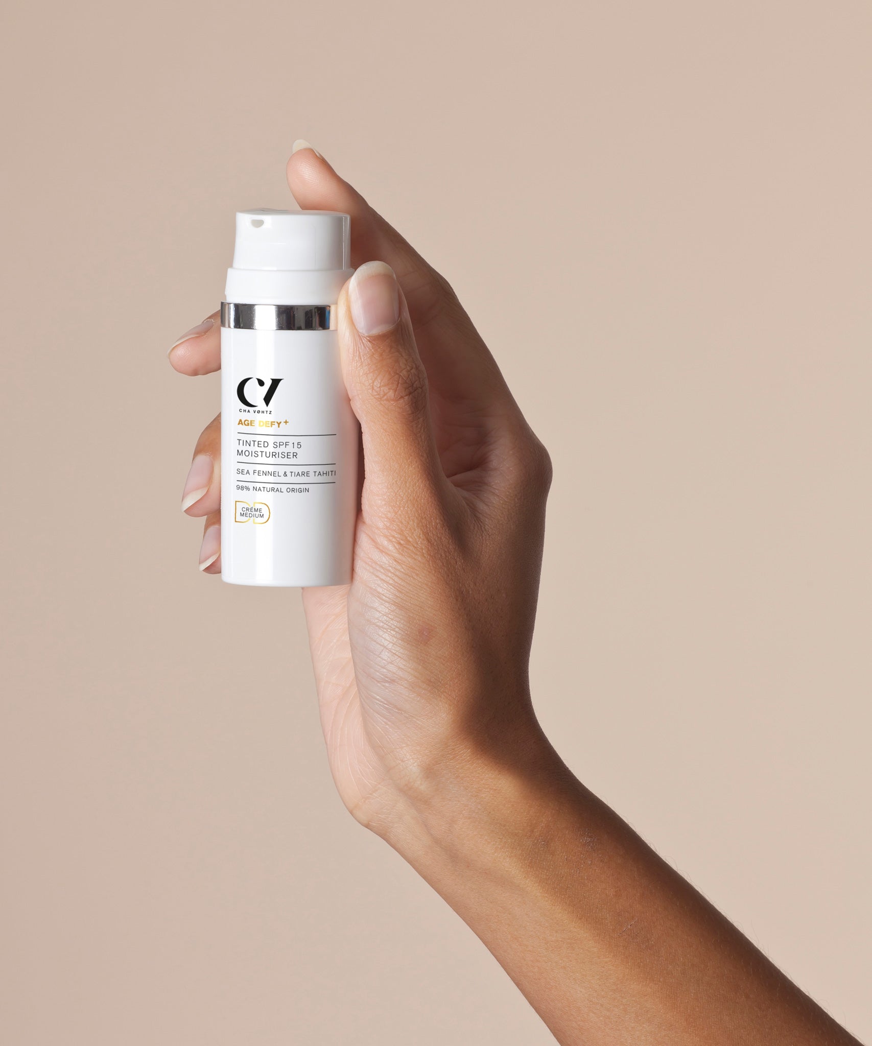 A Green People Light Tinted DD Moisturiser tube being held up against a beige background. 