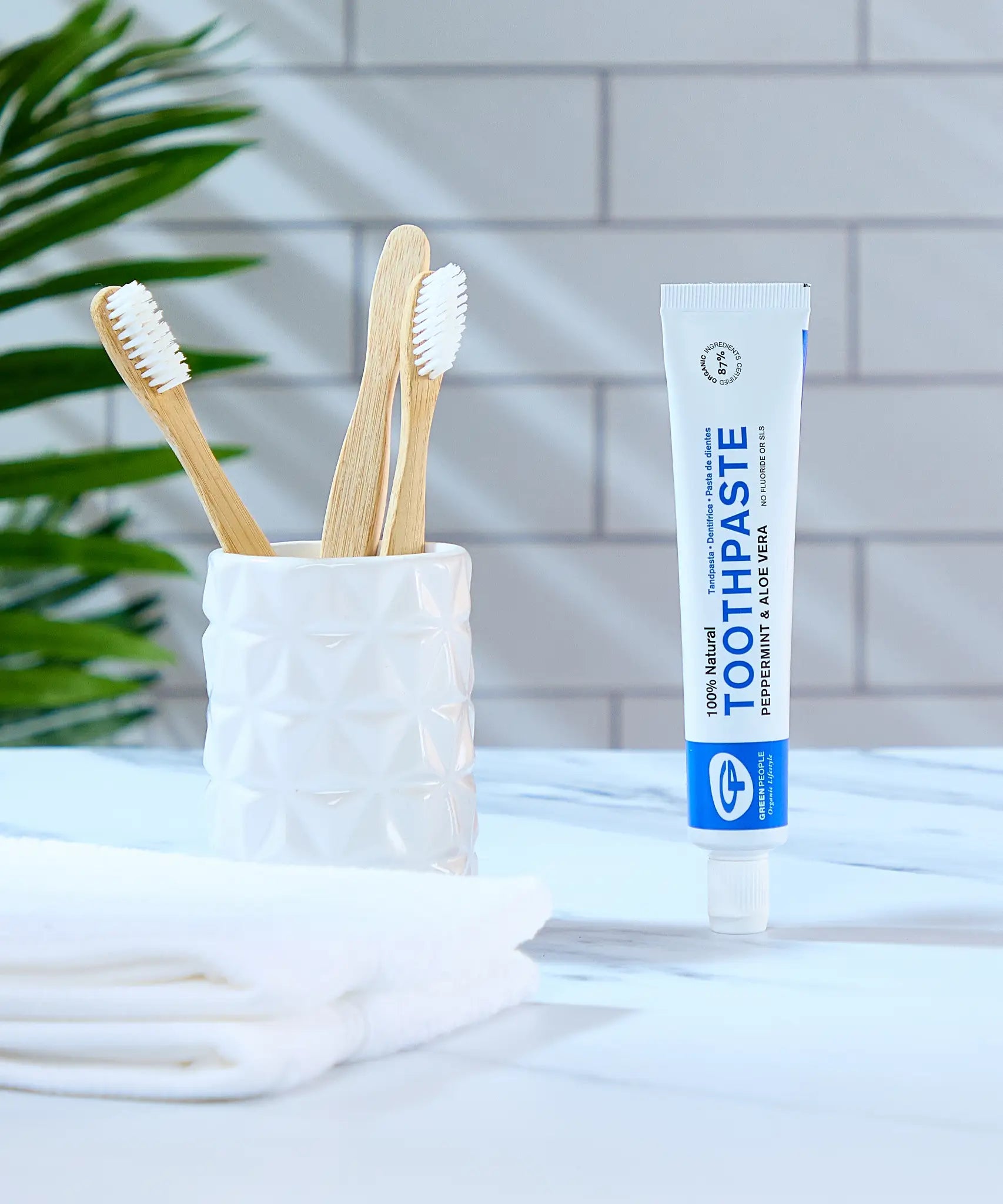 Organic People peppermint and aloe vera toothpaste tube in the bathroom next to a toothbrush holder 