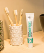 Tube of Organic People minty cool toothpaste next to a toothbrush holder