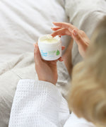 A close up of an adult's hand scooping some product out of the Organic Babies Mum & Baby Rescue Balm pot with their finger. 