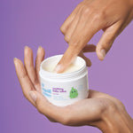 Organic Babies Soothing Baby Salve by Green People in a person's palm. The person is scooping some product from the pot with their finger.  