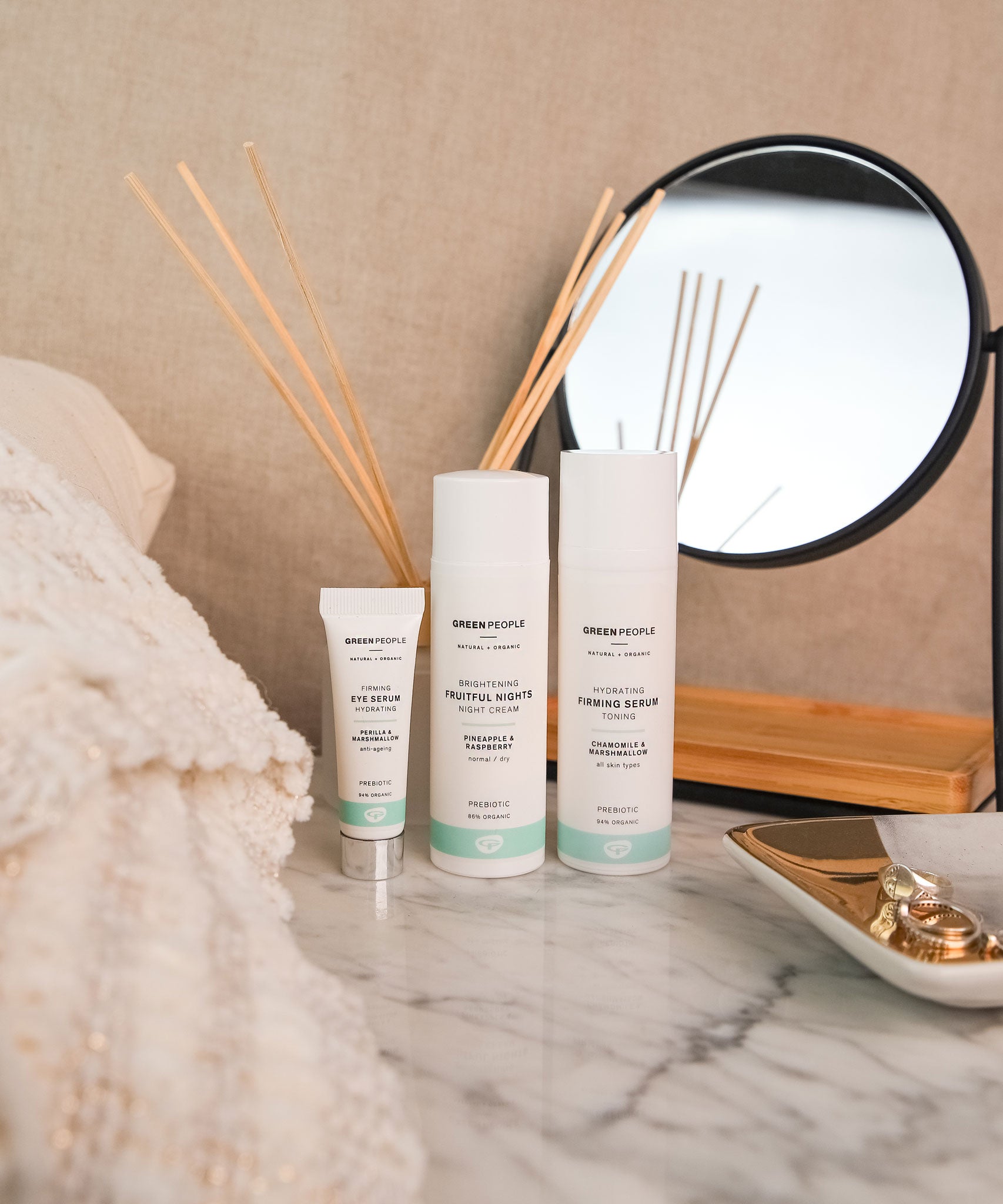 A collection of Green People organic facial care placed on a marble dressing table. A firming serum, a night cream and an eye serum. 